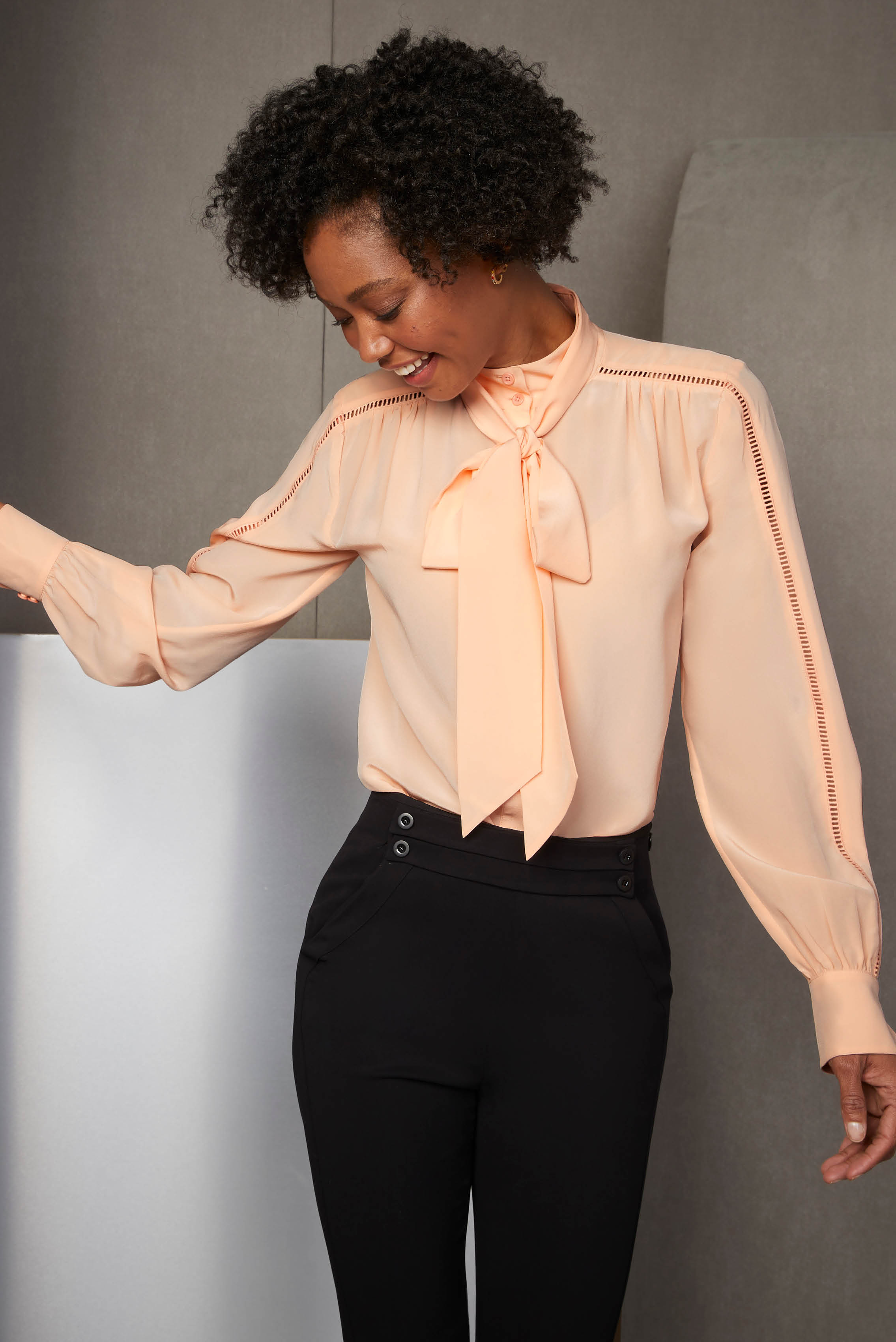 This silk crêpe de chine bow blouse in bright peach sets the tone for celebrating with its ladder stitch details, plus the shirring at the yoke and cuffs.