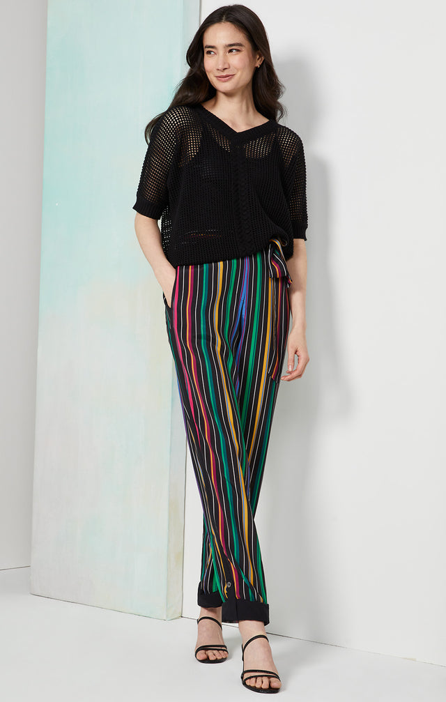 Lookbook photo of a model wearing the Parade pants, which is a colorful placed pinstripe convertible pants.